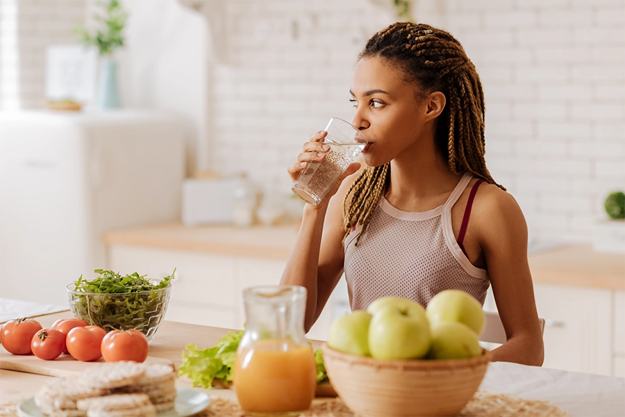  fit woman drinking water around fruit and vegetables on counter 